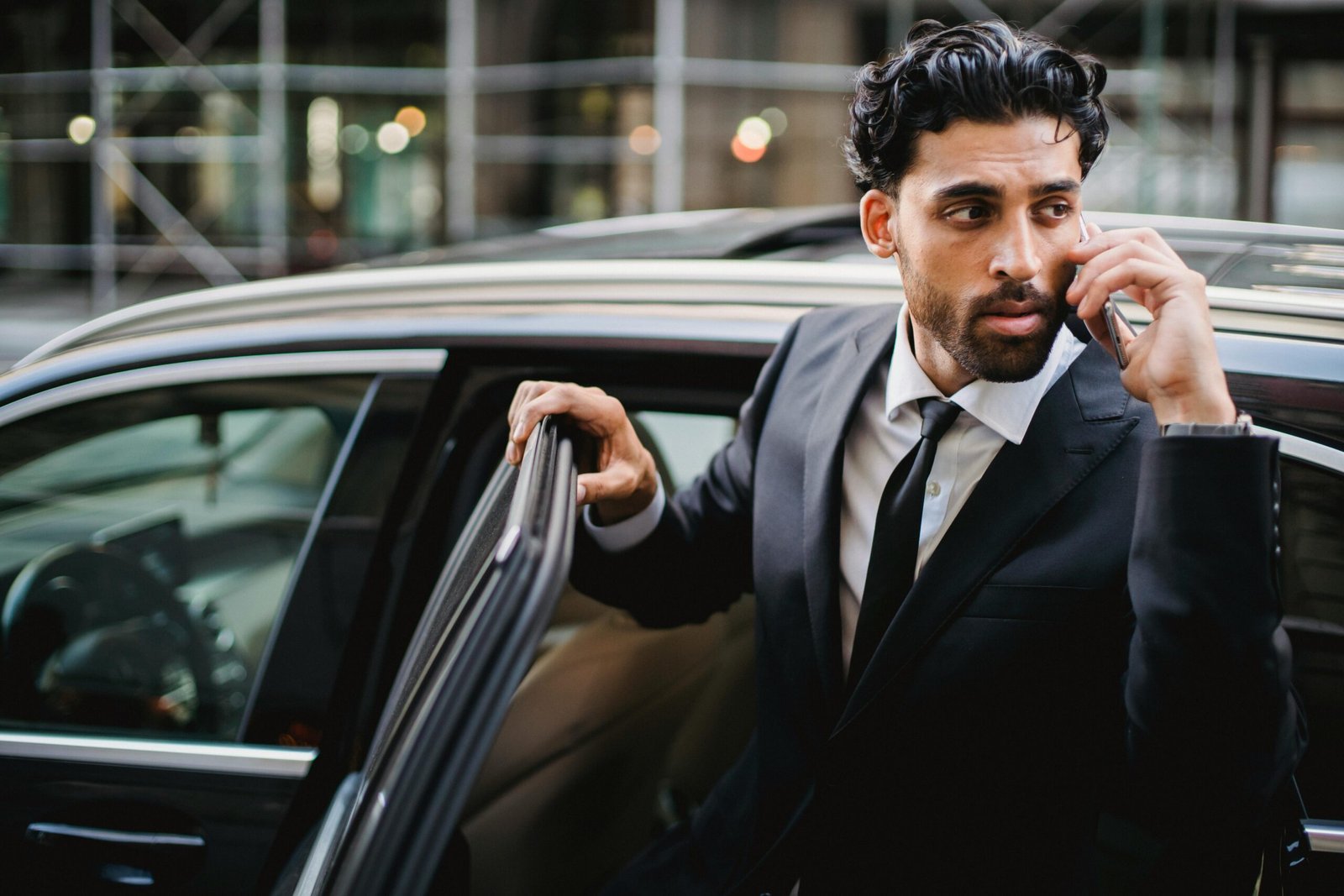 Confident businessman in a suit stepping out of a car while talking on the phone.